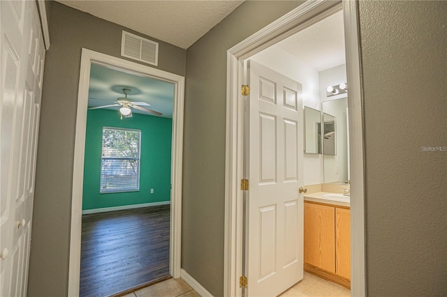corridor featuring a sink, visible vents, baseboards, and a textured ceiling