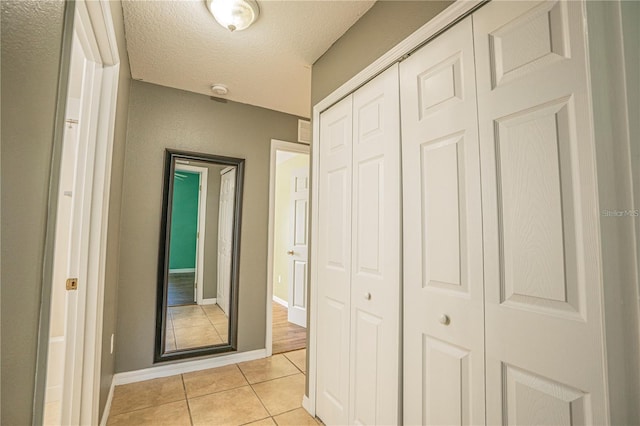 hallway with light tile patterned floors, baseboards, and a textured ceiling