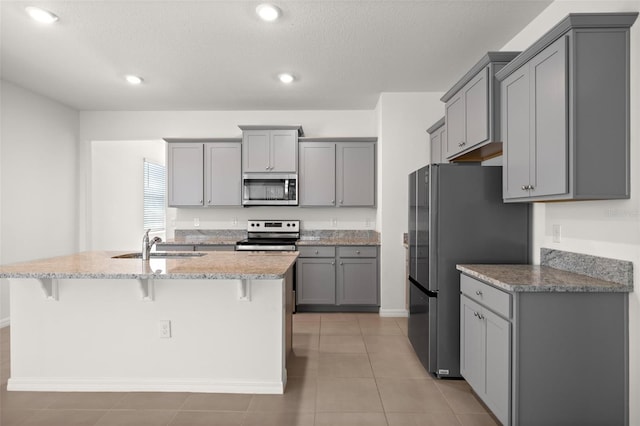 kitchen with a breakfast bar area, a sink, appliances with stainless steel finishes, and gray cabinets