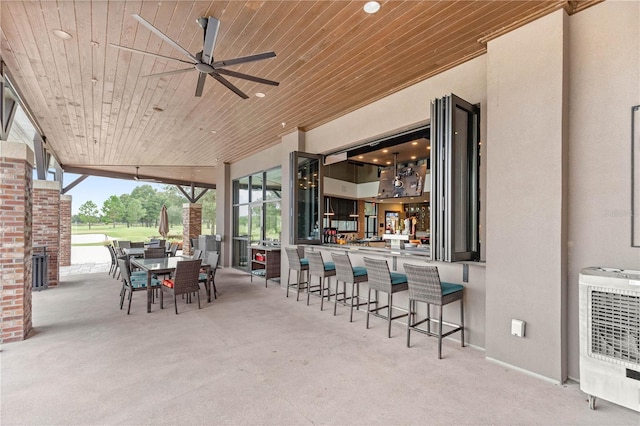 view of patio / terrace featuring ceiling fan, outdoor dining space, heating unit, and exterior bar