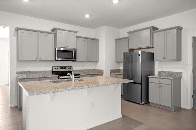 kitchen featuring gray cabinetry, a sink, an island with sink, and appliances with stainless steel finishes