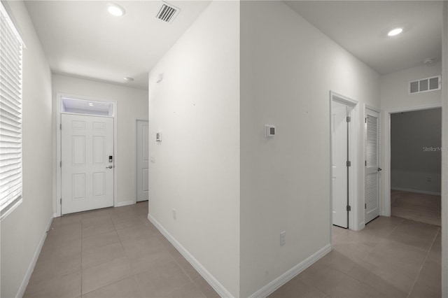 hall featuring baseboards, visible vents, and light tile patterned floors