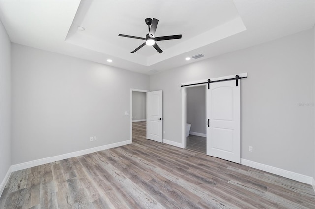 791 NE 150th Ave, Williston, FL 32696 - unfurnished bedroom with a raised ceiling, a barn door, wood finished floors, and visible vents