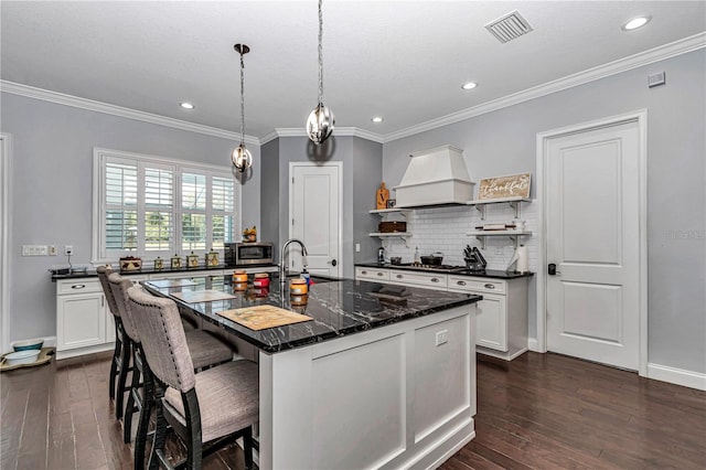 kitchen with backsplash, open shelves, visible vents, stainless steel microwave, and custom range hood