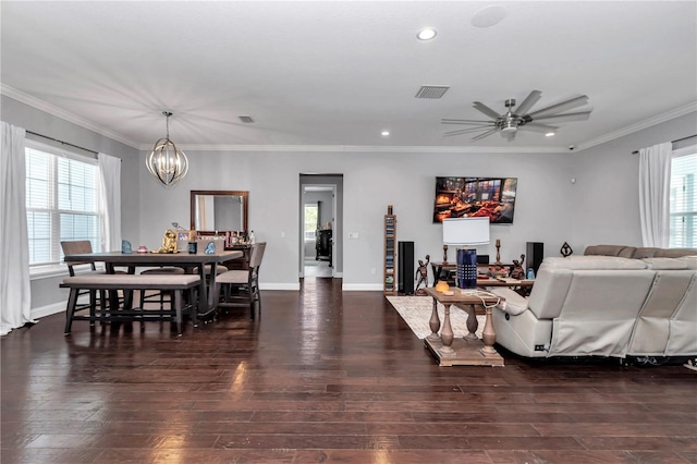 living room featuring ceiling fan with notable chandelier, dark wood finished floors, baseboards, visible vents, and ornamental molding