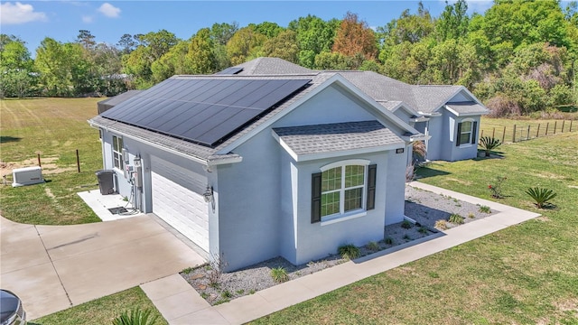ranch-style home with stucco siding, driveway, a front yard, solar panels, and a shingled roof