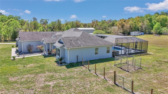rear view of property with stucco siding, a lawn, roof with shingles, and a lanai