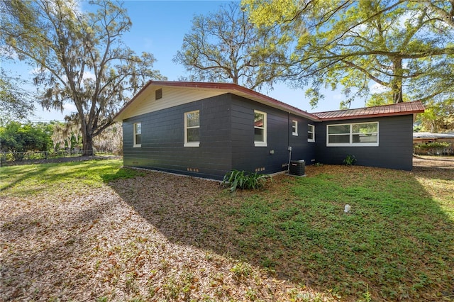 view of side of property with a lawn, fence, metal roof, crawl space, and central AC unit