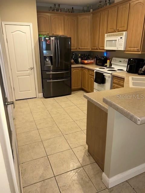 kitchen with a peninsula, white appliances, light countertops, a sink, and light tile patterned floors