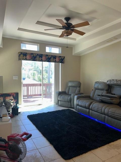 living area with ceiling fan, tile patterned floors, and a tray ceiling