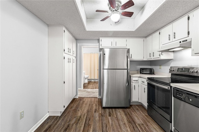 kitchen featuring stainless steel appliances, dark wood finished floors, a ceiling fan, under cabinet range hood, and a raised ceiling