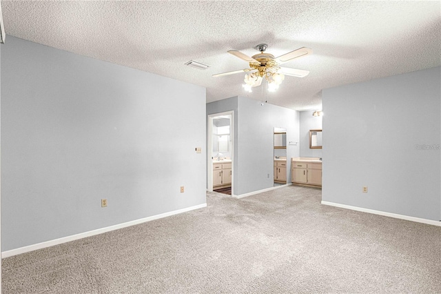 unfurnished bedroom with visible vents, light carpet, connected bathroom, baseboards, and a textured ceiling
