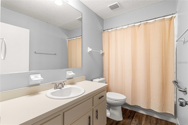 bathroom featuring a textured ceiling, toilet, visible vents, wood finished floors, and vanity