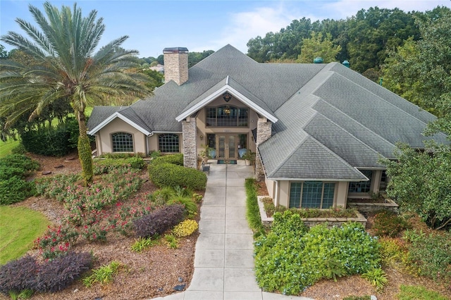 view of front of home featuring a chimney, stone siding, stucco siding, and french doors