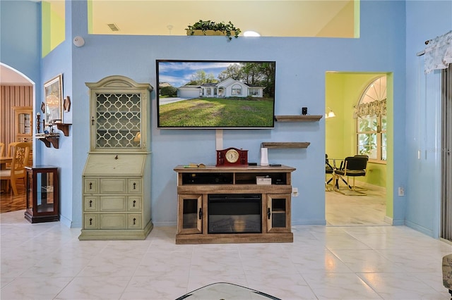 living room featuring arched walkways, visible vents, a high ceiling, and baseboards
