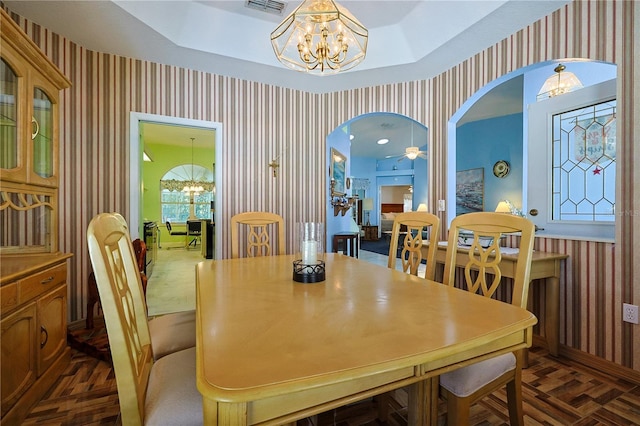 dining space with a chandelier, arched walkways, wallpapered walls, and a tray ceiling
