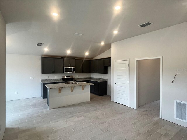 4504 SW 90th Lane Rd, Ocala, FL 34476 - kitchen with stainless steel microwave, lofted ceiling, a kitchen island with sink, light stone countertops, and light wood-style floors