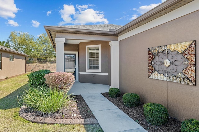 entrance to property featuring roof with shingles, a porch, stucco siding, and a yard