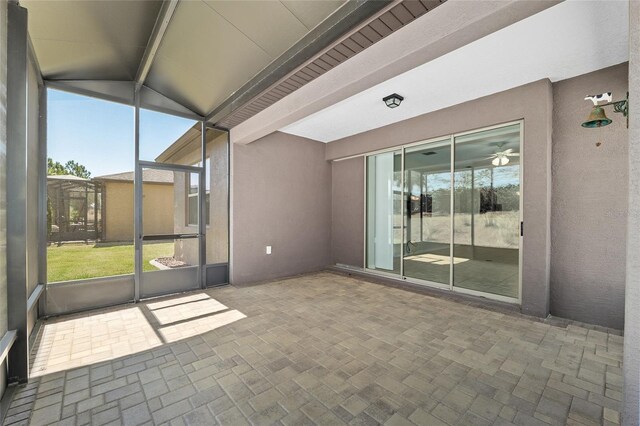 unfurnished sunroom with beamed ceiling, a ceiling fan, and a healthy amount of sunlight