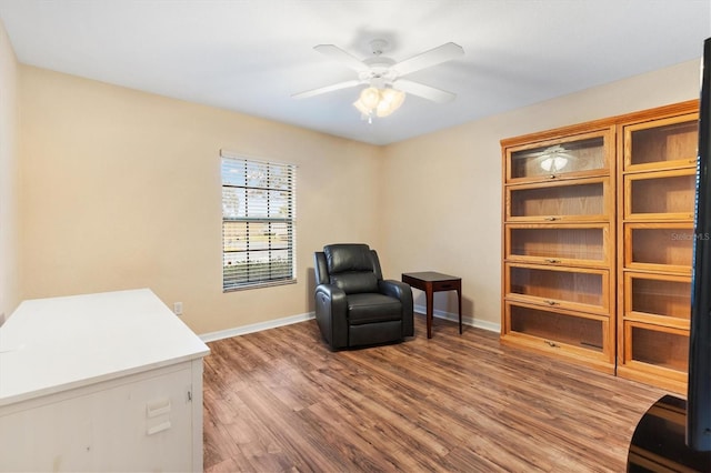 living area with a ceiling fan, wood finished floors, and baseboards