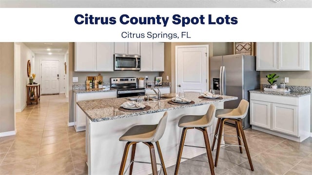 kitchen with a kitchen island with sink, appliances with stainless steel finishes, a kitchen breakfast bar, light tile patterned flooring, and a sink