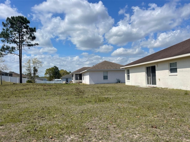 back of property featuring a yard, fence, and stucco siding