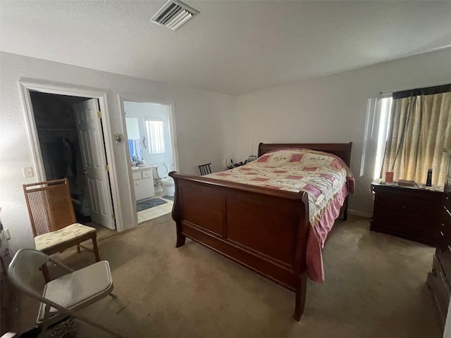 bedroom featuring visible vents, carpet, ensuite bath, and a walk in closet