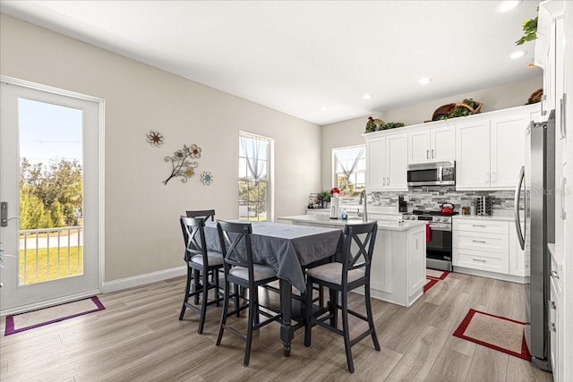 kitchen with decorative backsplash, a center island with sink, light wood-type flooring, white cabinets, and appliances with stainless steel finishes
