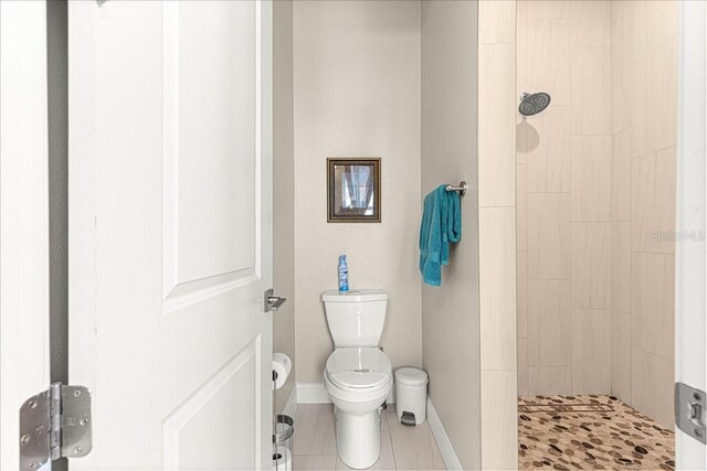 full bathroom with tile patterned flooring, baseboards, toilet, and tiled shower