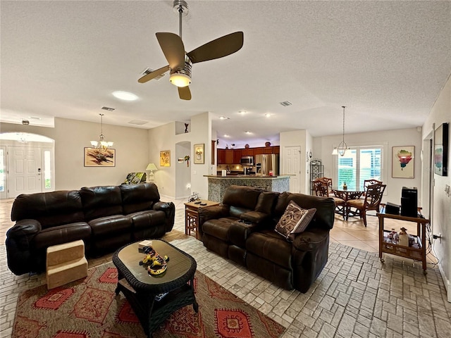 living area with ceiling fan with notable chandelier, visible vents, arched walkways, and a textured ceiling