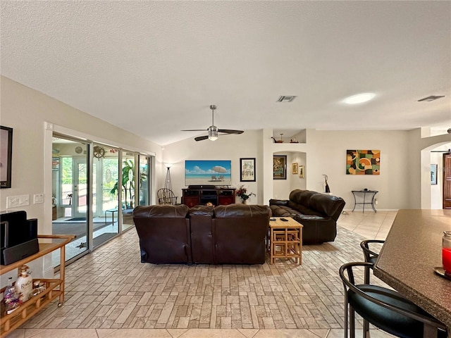 living room with lofted ceiling, a textured ceiling, arched walkways, visible vents, and a ceiling fan