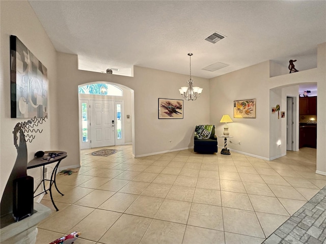 foyer entrance with light tile patterned floors, baseboards, a chandelier, arched walkways, and visible vents