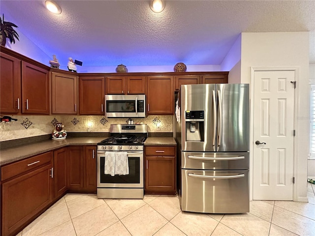 kitchen with a textured ceiling, dark countertops, light tile patterned floors, and stainless steel appliances