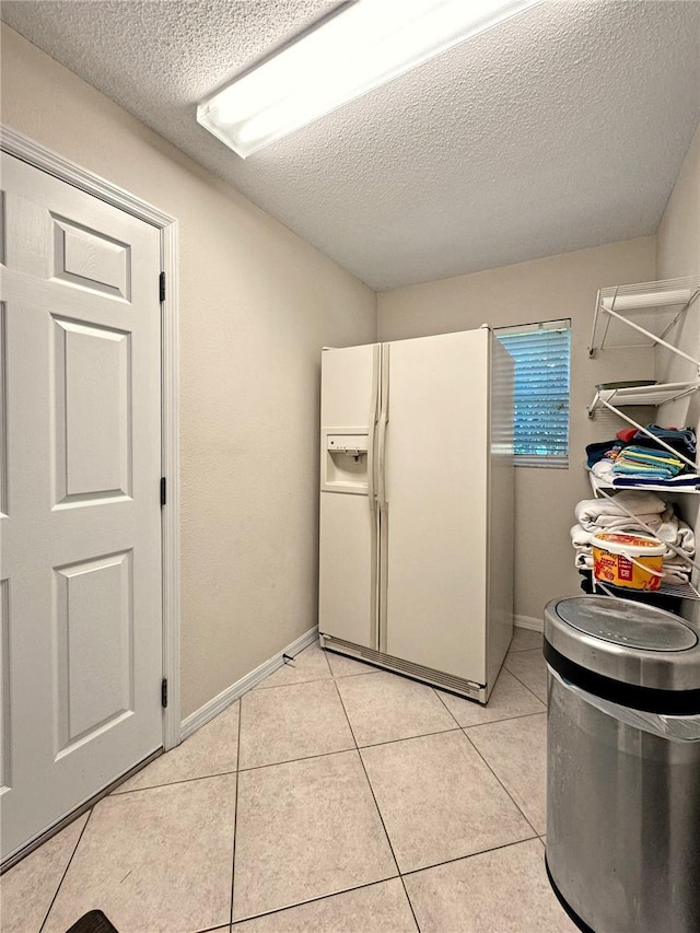 kitchen with white refrigerator with ice dispenser, a textured ceiling, baseboards, and light tile patterned floors