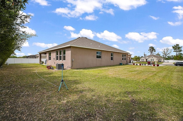 back of property with a yard, central AC unit, stucco siding, and fence