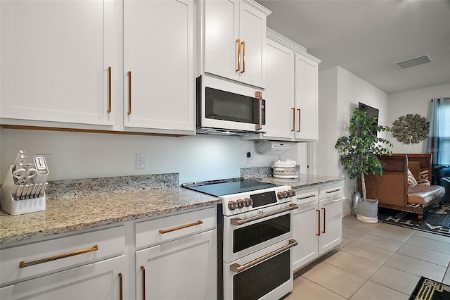 kitchen featuring white cabinetry, light tile patterned flooring, light stone counters, visible vents, and range with two ovens