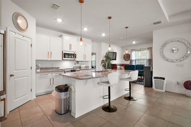 kitchen with white cabinetry, light tile patterned floors, a kitchen island with sink, visible vents, and light stone countertops