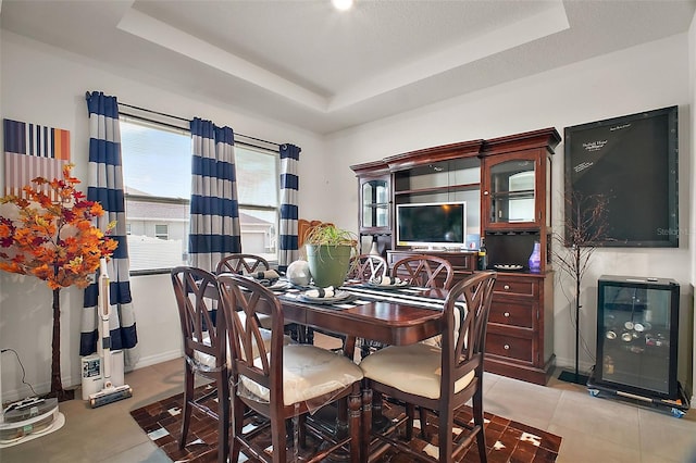 dining space with light tile patterned flooring, a tray ceiling, and baseboards