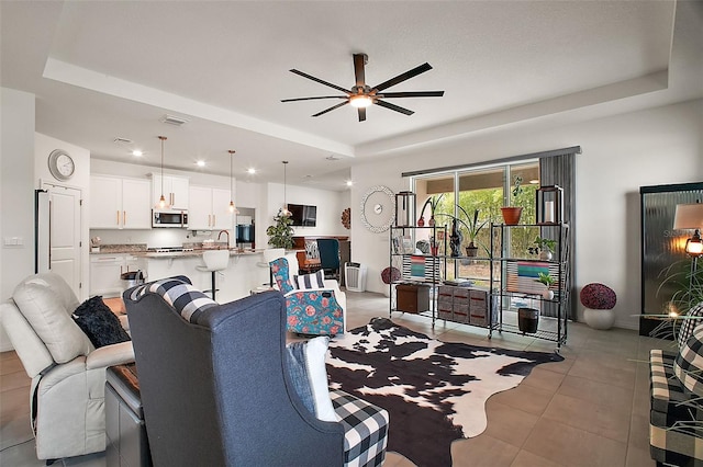 living room featuring a ceiling fan, light tile patterned flooring, a tray ceiling, and visible vents