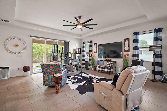 tiled living area with a ceiling fan, a tray ceiling, and visible vents