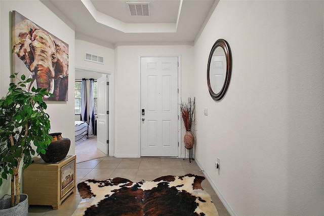 entryway with baseboards, visible vents, light tile patterned floors, and a raised ceiling