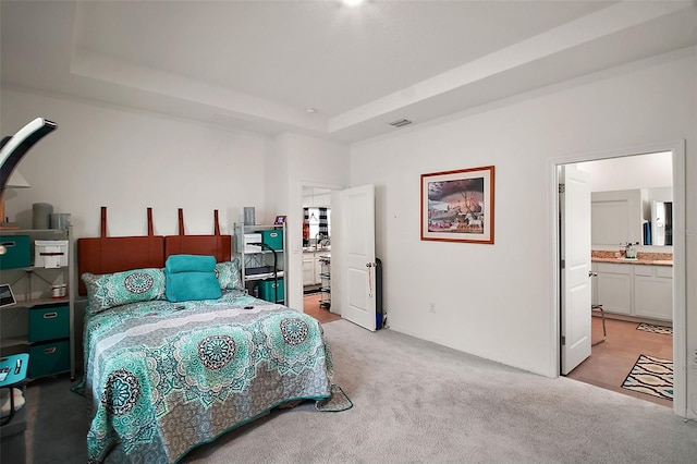 bedroom with light carpet, a tray ceiling, ensuite bath, and visible vents