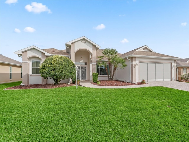 view of front of property featuring a front yard, decorative driveway, stucco siding, and an attached garage