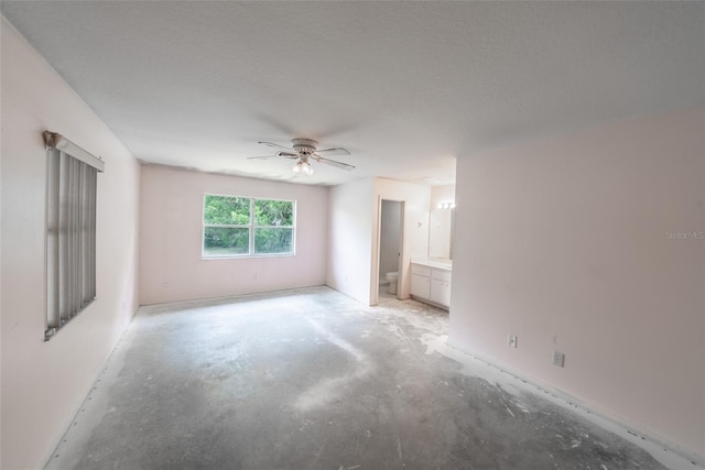 unfurnished bedroom with concrete flooring, a textured ceiling, ensuite bathroom, and ceiling fan