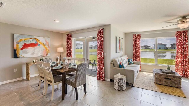 tiled dining space with a textured ceiling, baseboards, visible vents, a water view, and ceiling fan