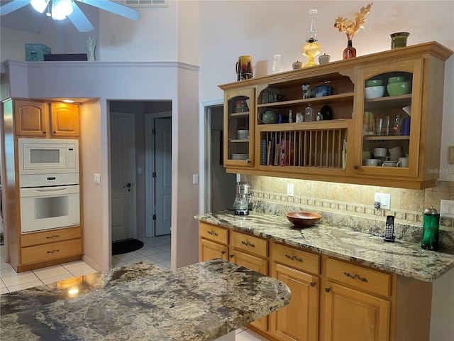 kitchen featuring backsplash, light stone countertops, light tile patterned floors, white appliances, and ceiling fan