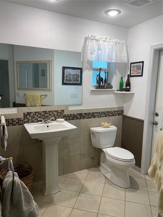 bathroom featuring toilet, a textured ceiling, tile patterned floors, visible vents, and wainscoting