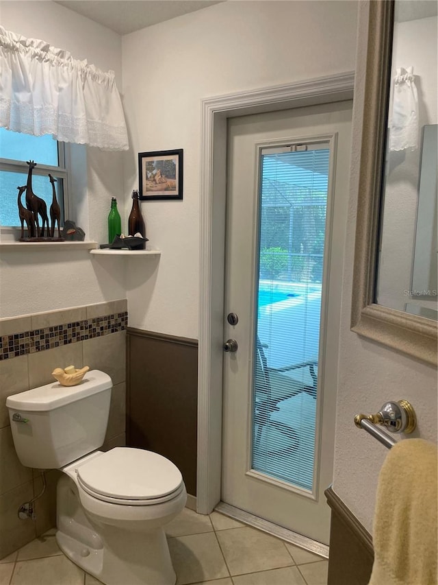 bathroom with tile patterned flooring, toilet, tile walls, and wainscoting