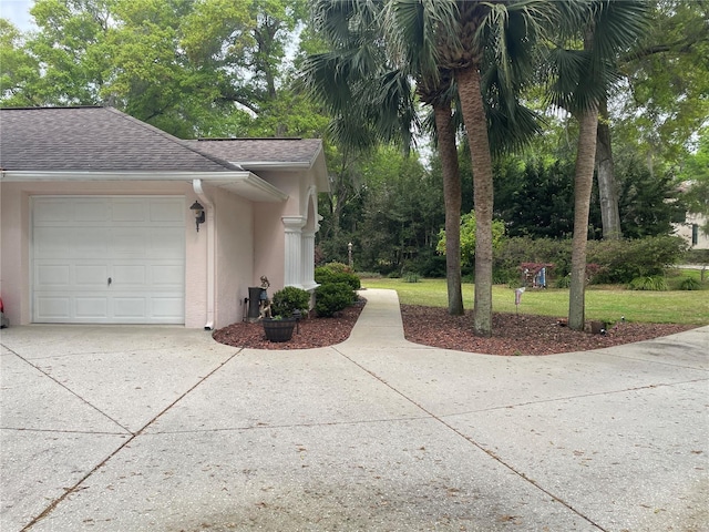 view of side of property featuring concrete driveway, stucco siding, an attached garage, a shingled roof, and a yard