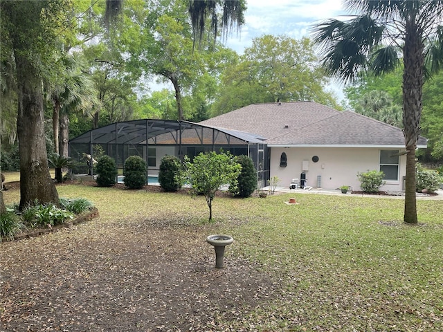 back of house featuring glass enclosure, a lawn, a shingled roof, and stucco siding